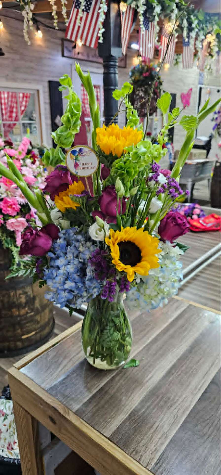 Tall birthday arrangement with sunflowers, hydrangea, and bells of Ireland