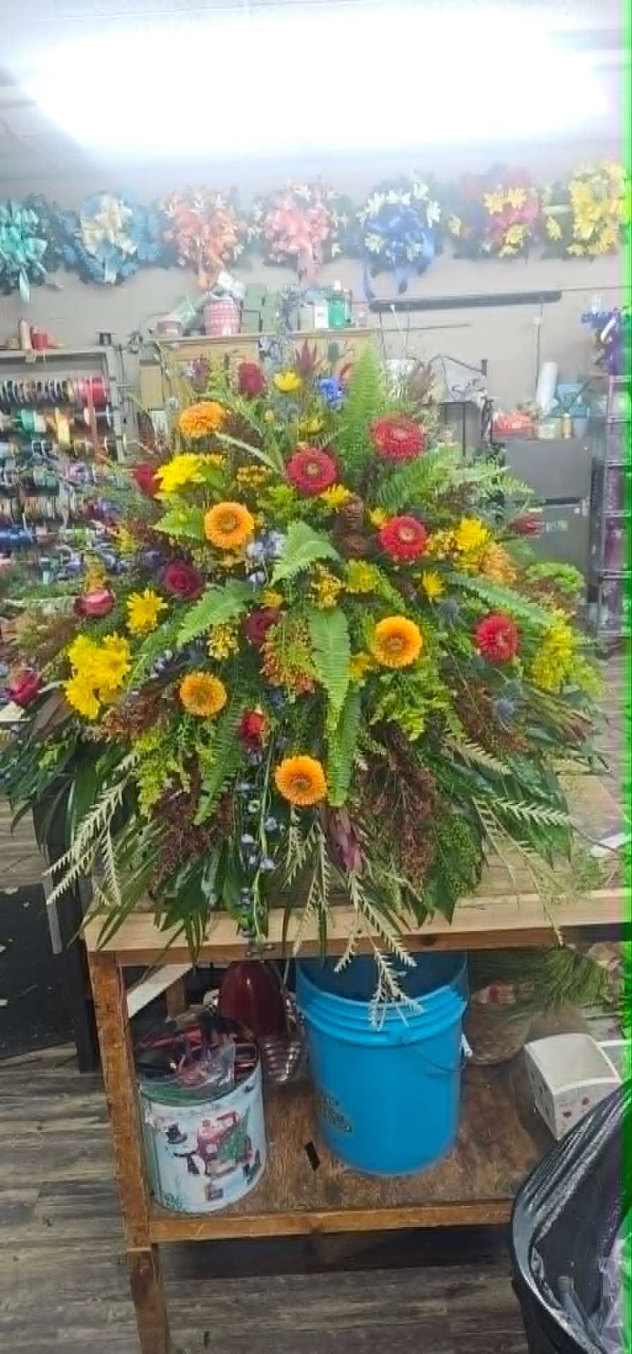 Vibrant standing memorial spray with orange gerberas, red zinnias, and fern