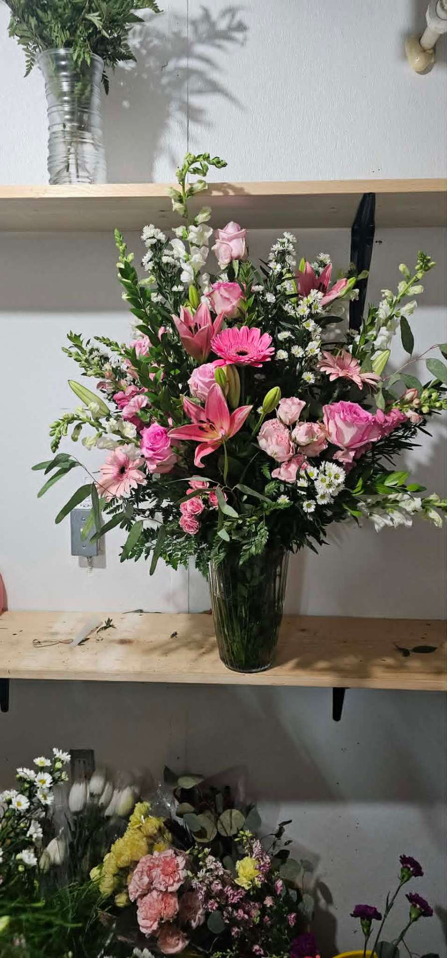 Tall pink rose, lily, and gerbera arrangement on a wooden shelf